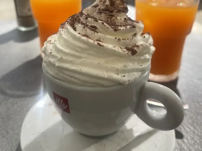 Cappuccino illy coiffé de chantilly et cacao, servi avec un jus d'orange frais